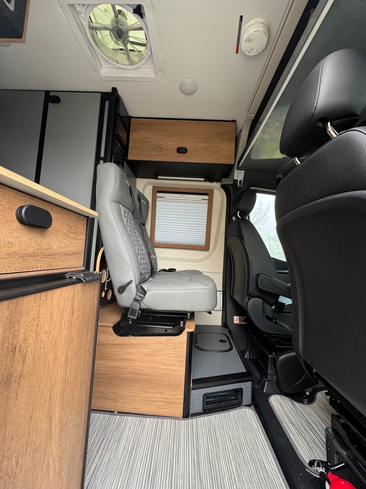 RV rental interior with a gray swivel seat, wooden storage, ceiling fan, and textured flooring, ready for travel.