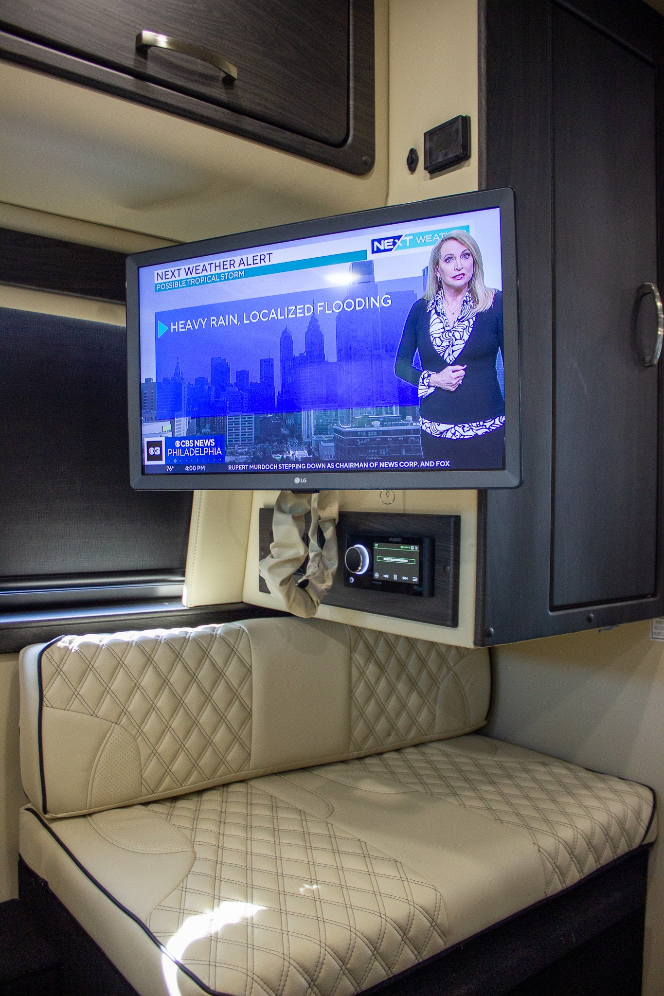 Luxury rv rental interior with TV showing a weather alert, an entertainment system, and comfortable upholstered seating.