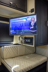 Luxury rv rental interior with TV showing a weather alert, an entertainment system, and comfortable upholstered seating.