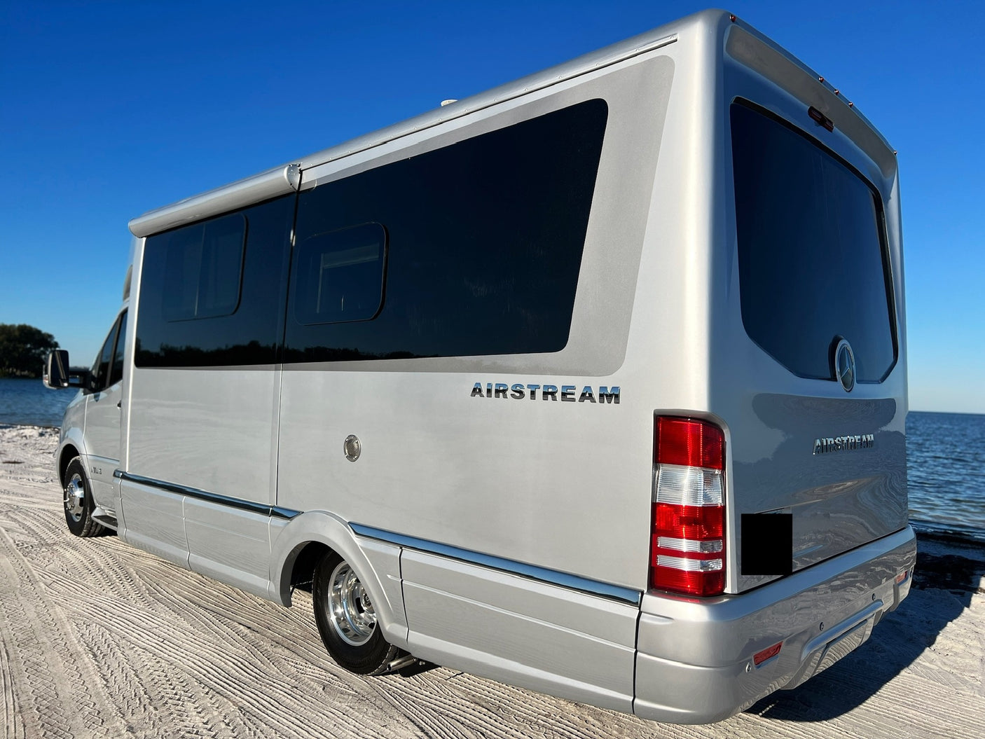Experience the open road with this stunning silver Airstream rv rental, parked on a sandy shore by blue water.