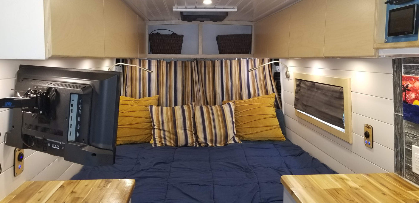 Step inside this comfortable RV rental camper van, featuring a cozy bed, wall-mounted TV, smart storage, and warm wood accents.