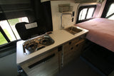 This RV rental camper van features a compact kitchen with a two-burner stove, sink, and a cozy bed area.