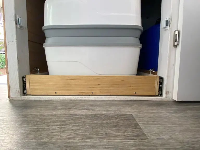 Compact white portable toilet on a slide-out tray, neatly stored in an RV cabinet for your RV rental.