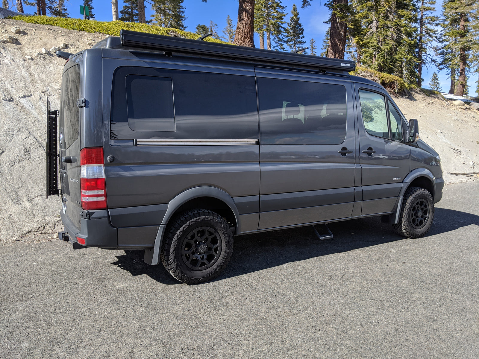 Gray Mercedes Sprinter camper van, an RV rental, ready for exploration with off-road tires and rooftop awning.
