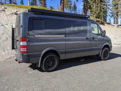 Gray Mercedes Sprinter camper van, an RV rental, ready for exploration with off-road tires and rooftop awning.