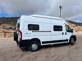 White Winnebago Solis camper van for rv rental parked on gravel, backed by mountains and a cloudy sky. Ideal for adventure travel.
