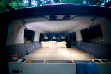 Inside a cozy RV rental campervan: custom bed platform with pillows, storage, and ambient lighting, perfect for van life.