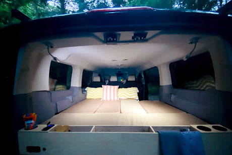 Inside a cozy RV rental campervan: custom bed platform with pillows, storage, and ambient lighting, perfect for van life.