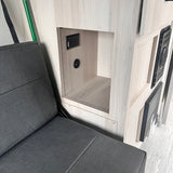 RV rental: Dark grey upholstered seat next to a wood-paneled interior with built-in AC and USB charging ports.