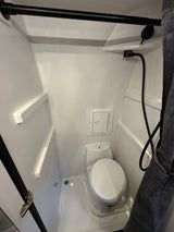Inside an RV rental: a clean, compact wet bath featuring a toilet, handheld shower, and integrated shelves.
