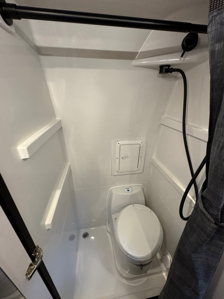 Inside an RV rental: a clean, compact wet bath featuring a toilet, handheld shower, and integrated shelves.