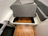 RV rental interior view: grey upholstered cushions, open storage under seating with wood floor, and a silver Lagun table base.