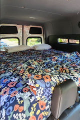 RV rental interior featuring a comfy van bed with a colorful floral quilt and pillows, ready for travels.
