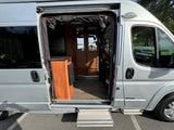 Silver RV rental van, side door open with step extended, showing its welcoming wood interior.