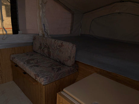 Cozy RV rental interior: patterned bench, bed, and canvas walls. Features an 'EXIT' sign & wood paneling.