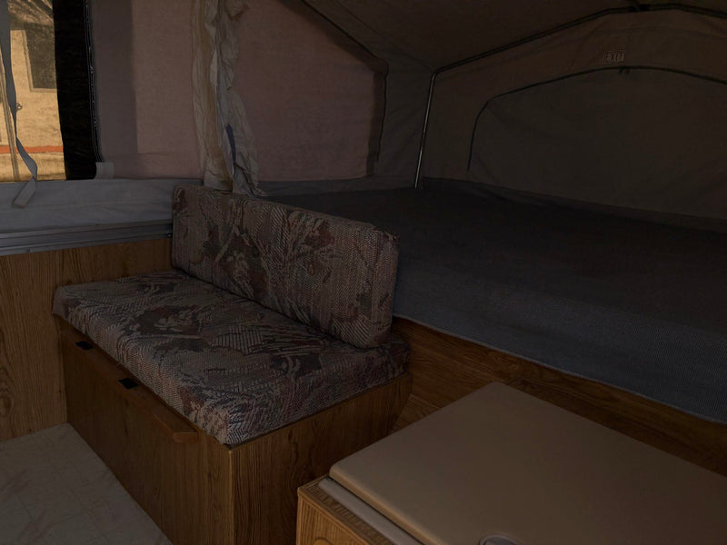 Cozy RV rental interior: patterned bench, bed, and canvas walls. Features an 'EXIT' sign & wood paneling. — photo 7