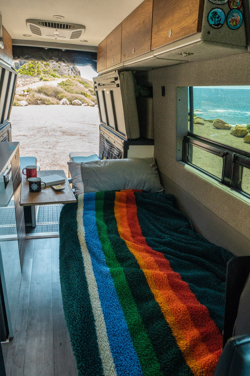 Cozy RV rental interior with bed, mugs, and a view of the ocean & landscape. — photo 5
