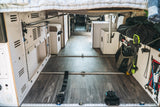 An RV rental's versatile interior shows modular white storage, L-track flooring, and various gear secured under a bed.