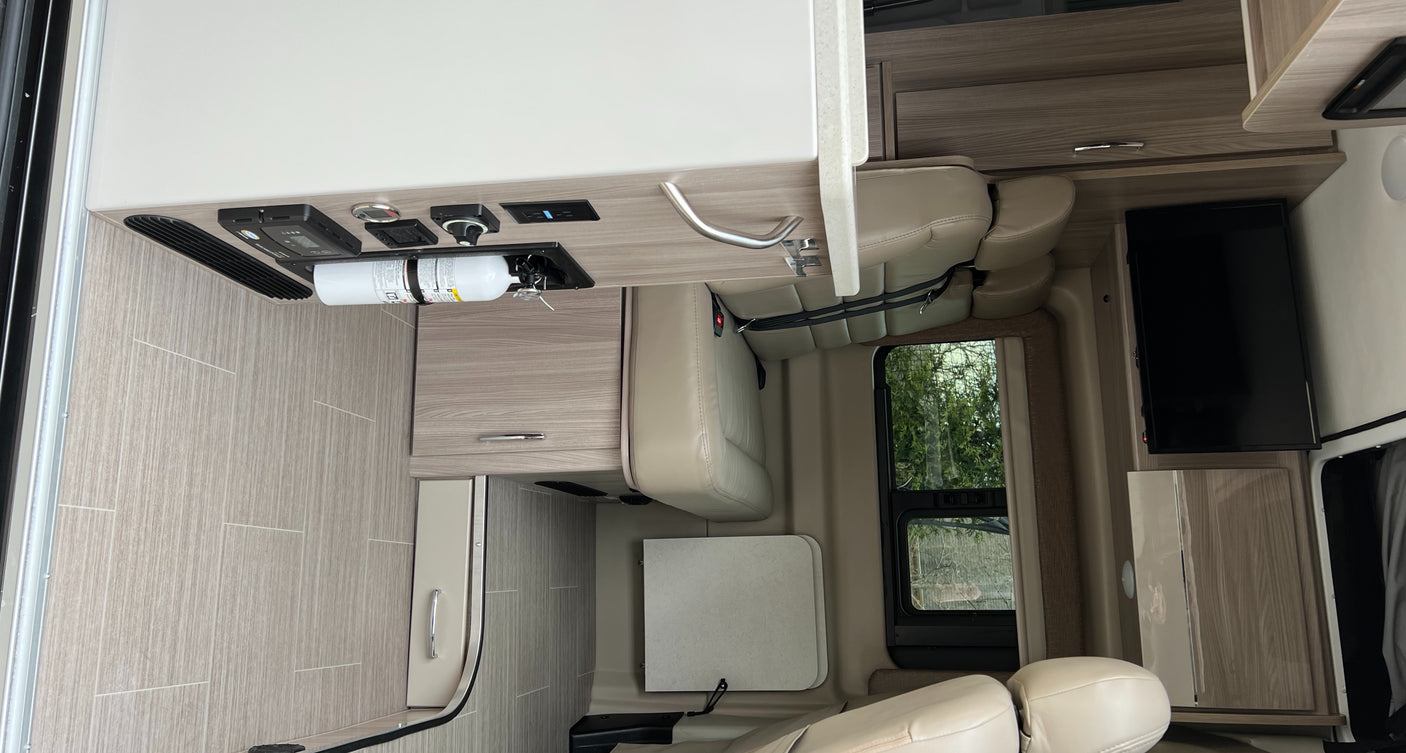 Spacious RV rental interior with a light-colored dinette, wood accents, control panel, and wall-mounted TV.