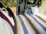 Comfortable RV rental interior with a bed, blankets, pillows, and a nature view. Ideal for road trip camping.