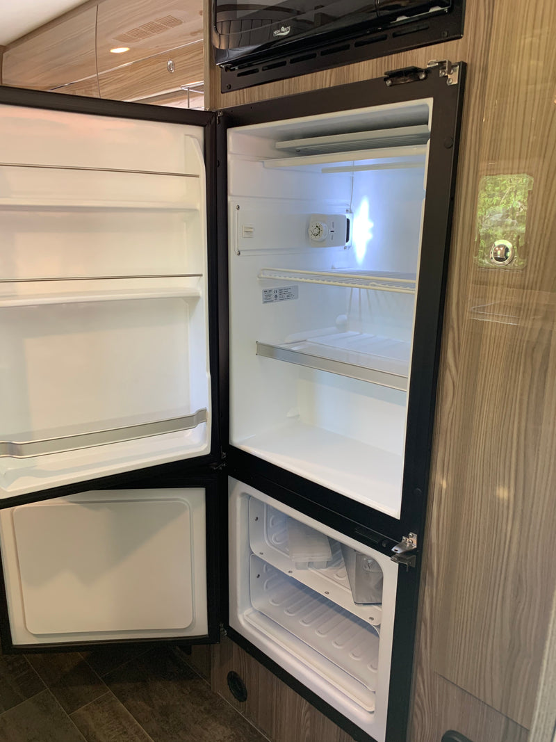 An open, empty RV rental refrigerator and bottom freezer with white interior, ideal for travel food storage. — photo 15