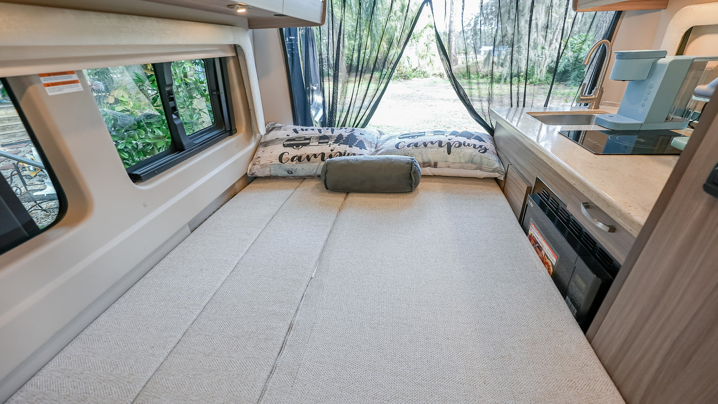 Cozy RV rental interior with a comfy bed, compact kitchen, and views of nature through the mesh screen at the back.