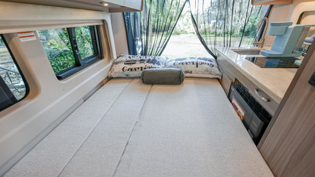 Cozy RV rental interior with a comfy bed, compact kitchen, and views of nature through the mesh screen at the back.