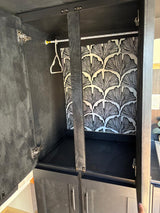 Stylish black cabinet in RV rental, featuring a hanging rod, hanger, and ginkgo leaf wallpaper for clever storage.