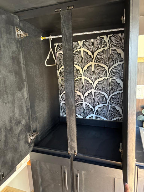 Stylish black cabinet in RV rental, featuring a hanging rod, hanger, and ginkgo leaf wallpaper for clever storage.