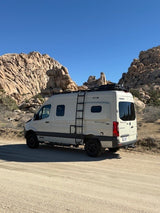 Your next RV rental adventure: A beige camper van parked on a dirt road with large desert rock formations.
