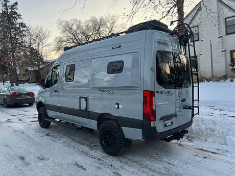 Gray Winnebago Revel Sprinter camper van (rv rental option) on a snowy street, ready for winter adventure.