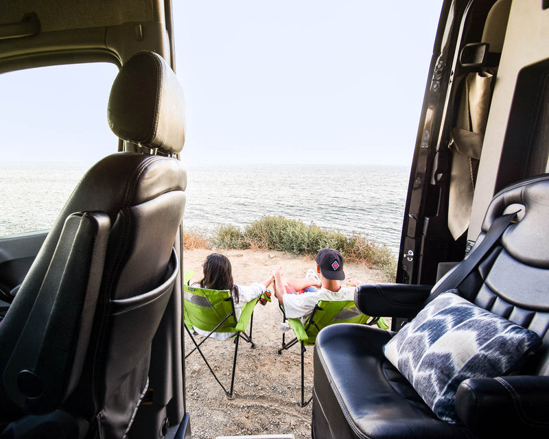 RV rental view: Couple enjoys ocean vista from camping chairs. Perfect van life escape.|A person relaxes in an RV rental — photo 1