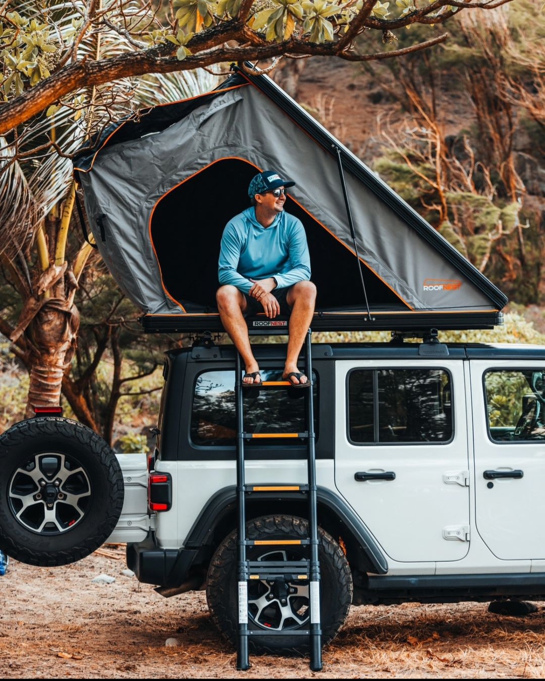  mountains behind. Ideal rv rental for Maui camping.|Man on a grey rooftop tent atop a white Jeep with a ladder