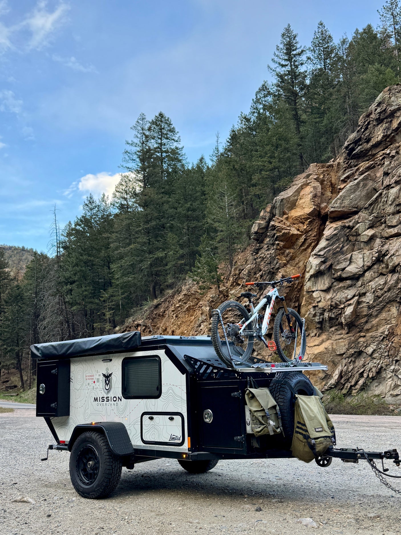Overland trailer RV rental with a mountain bike, parked by a rocky mountain road. Perfect for adventure travel.