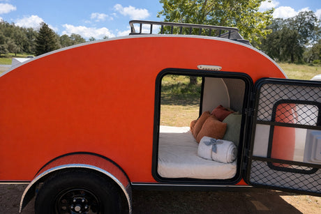 Vibrant orange teardrop RV rental, door open to reveal a comfortable bed. Ready for your next camping trip.