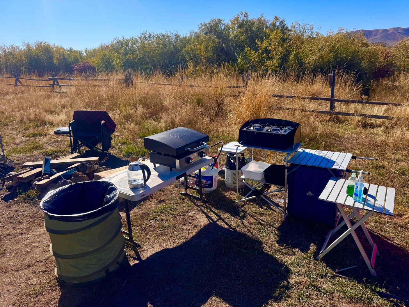 Outdoor camp kitchen setup for an RV rental trip: portable griddle, stove, tables, and supplies in a sunny field.