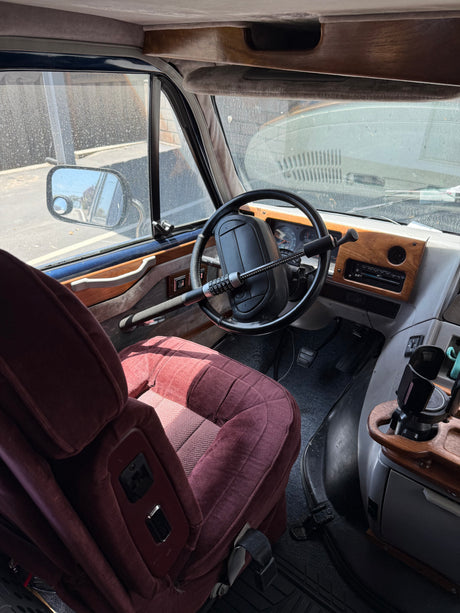 Inside this RV rental: driver's seat, steering wheel with security lock, dashboard, and custom wood trim.