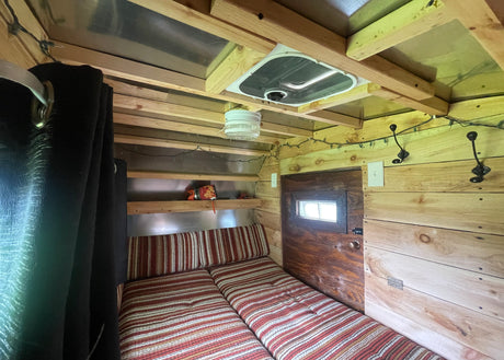 This inviting RV rental features a cozy striped bed, natural wood accents, shelves, and a ceiling fan.
