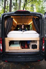 Woman reading in a converted van's cozy interior, featuring bed & storage. A perfect RV rental for van life.