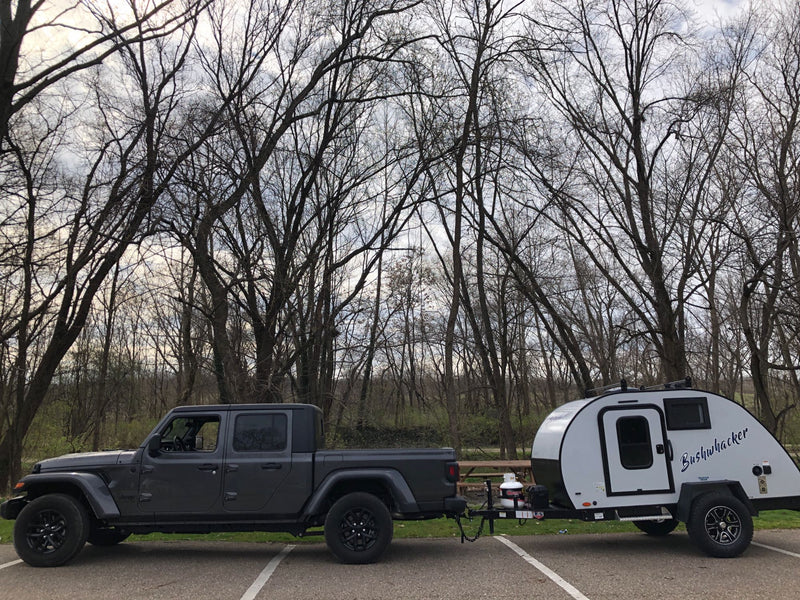 A gray Jeep Gladiator pickup tows a compact, white Bushwhacker teardrop travel trailer, perfect for an RV rental adventure. — photo 2