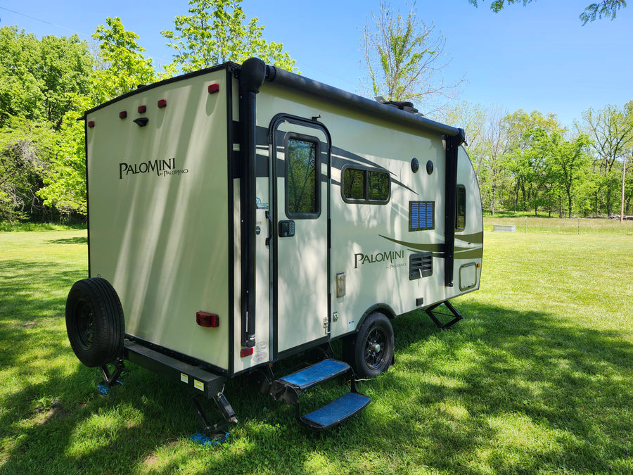 Discover this Palomini travel trailer, an ideal RV rental. Parked in a sunny green field, ready for outdoor camping adventures.