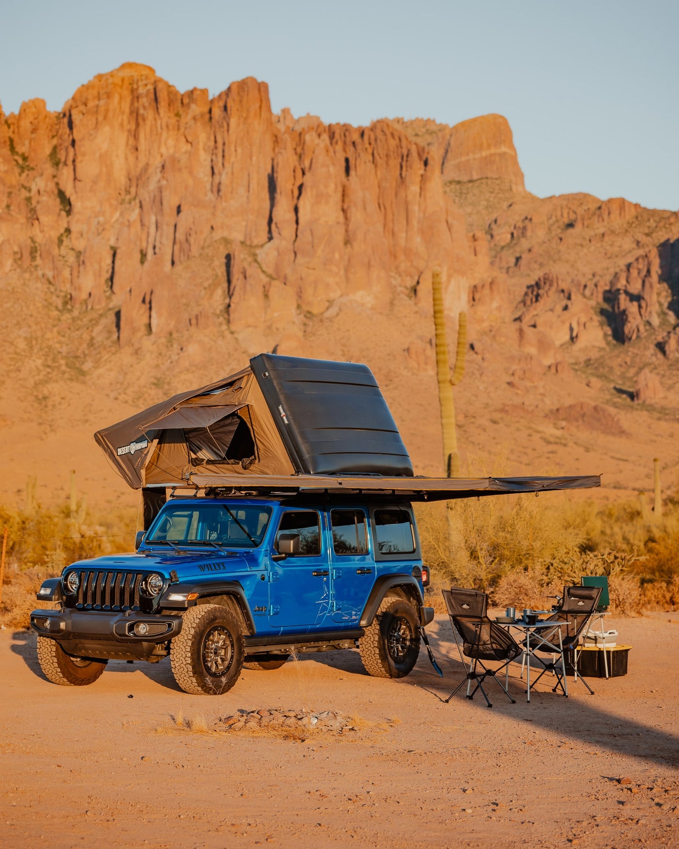Blue Jeep with a rooftop tent & awning fully deployed in a desert camp. Mountains & cacti frame this ideal RV rental overlanding scene. — photo 5