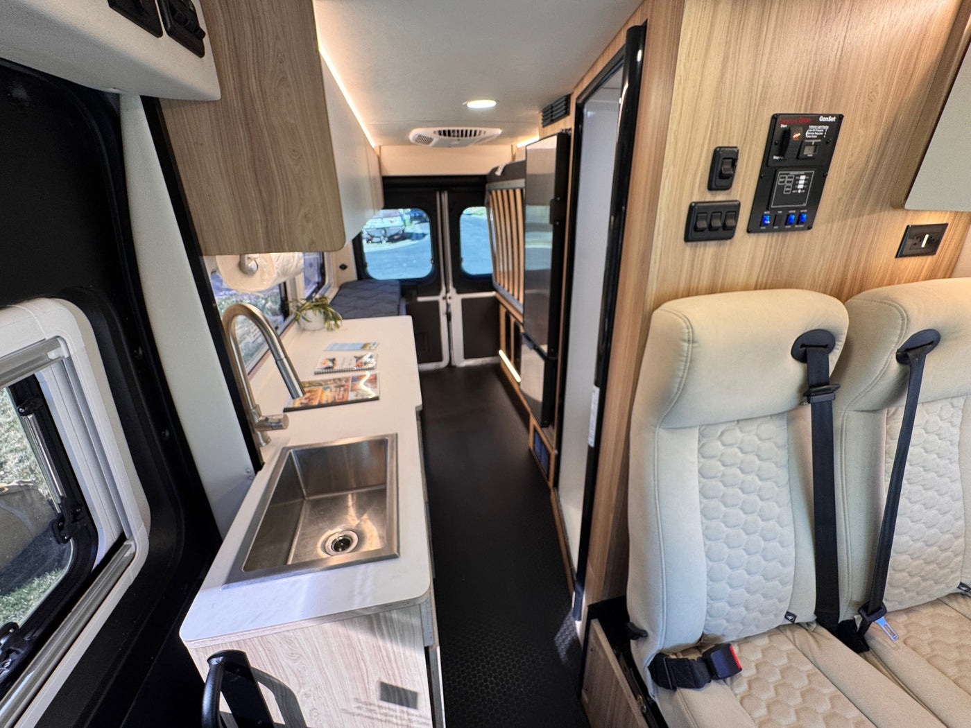 Spacious RV rental interior featuring a kitchenette with sink, comfortable seating, and a generator control panel on the wall. — photo 13