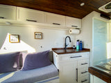 Bright RV rental interior features a mini kitchen with sink, white cabinets, wood ceiling, and cozy seating.