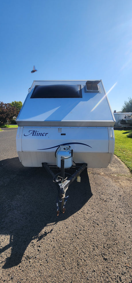 Front view of a white A-liner pop-up camper, showing its propane tank and hitch. Ready for an RV rental adventure on a bright, sunny day.