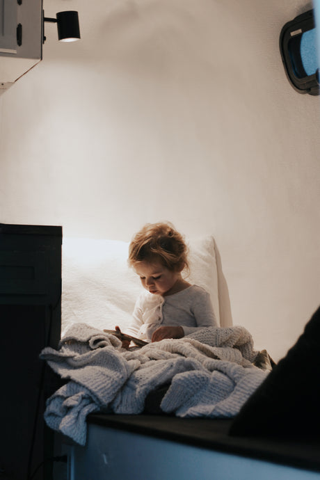 Cozy rv rental interior: A young child, bundled in a blanket, looks at a device, illuminated by a warm lamp.