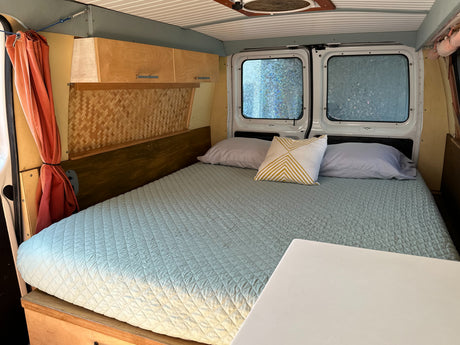 Cozy rv rental interior: large light blue bed, wood cabinets, unique bamboo-patterned wall, and private frosted windows.
