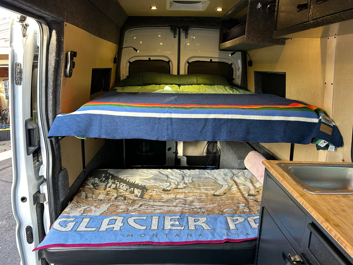 RV rental: Cozy camper van interior with stacked beds, a Glacier Park blanket, and a compact sink. — photo 6