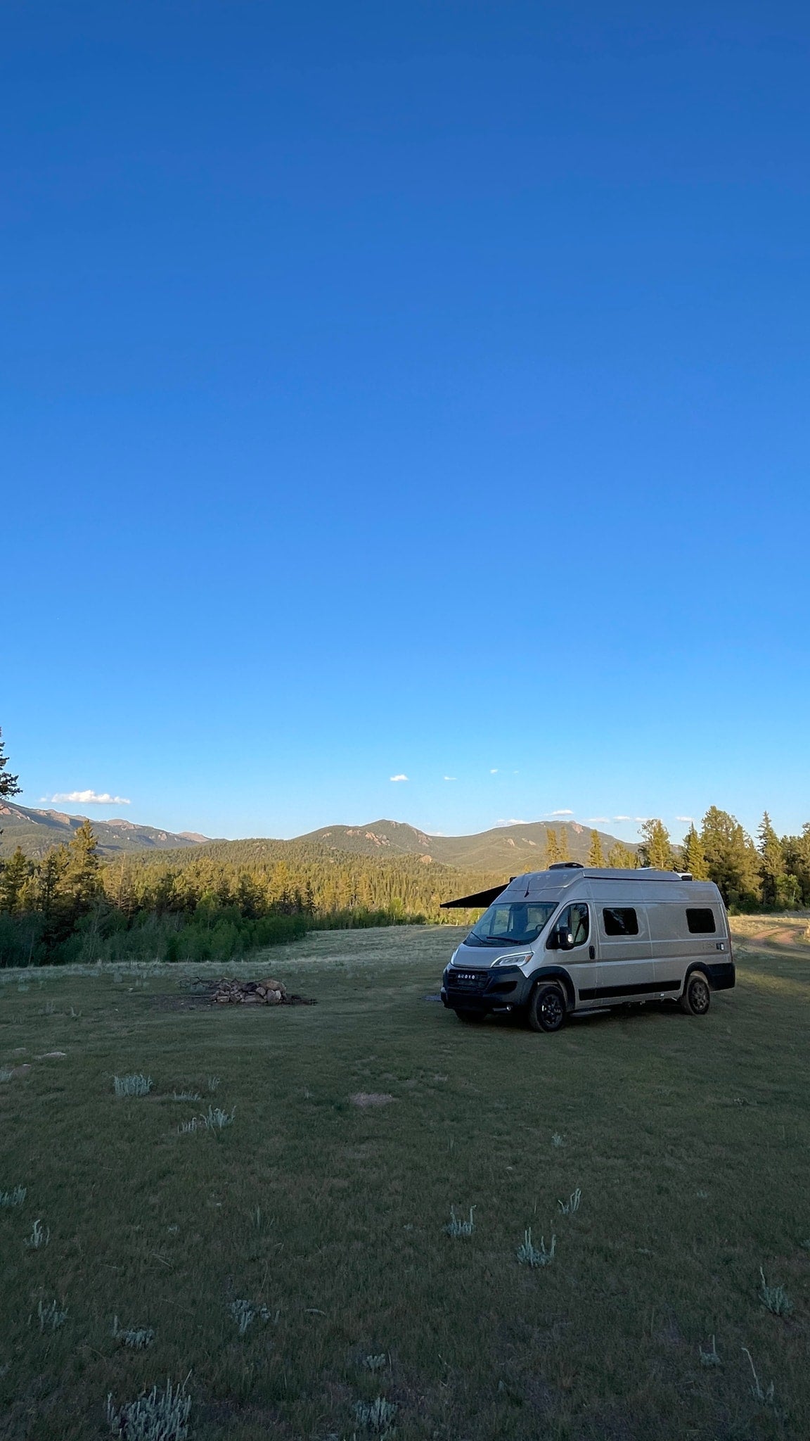 RV rental boondocking: a grey camper van with awning in a vast mountain field under a clear blue sky. — photo 18