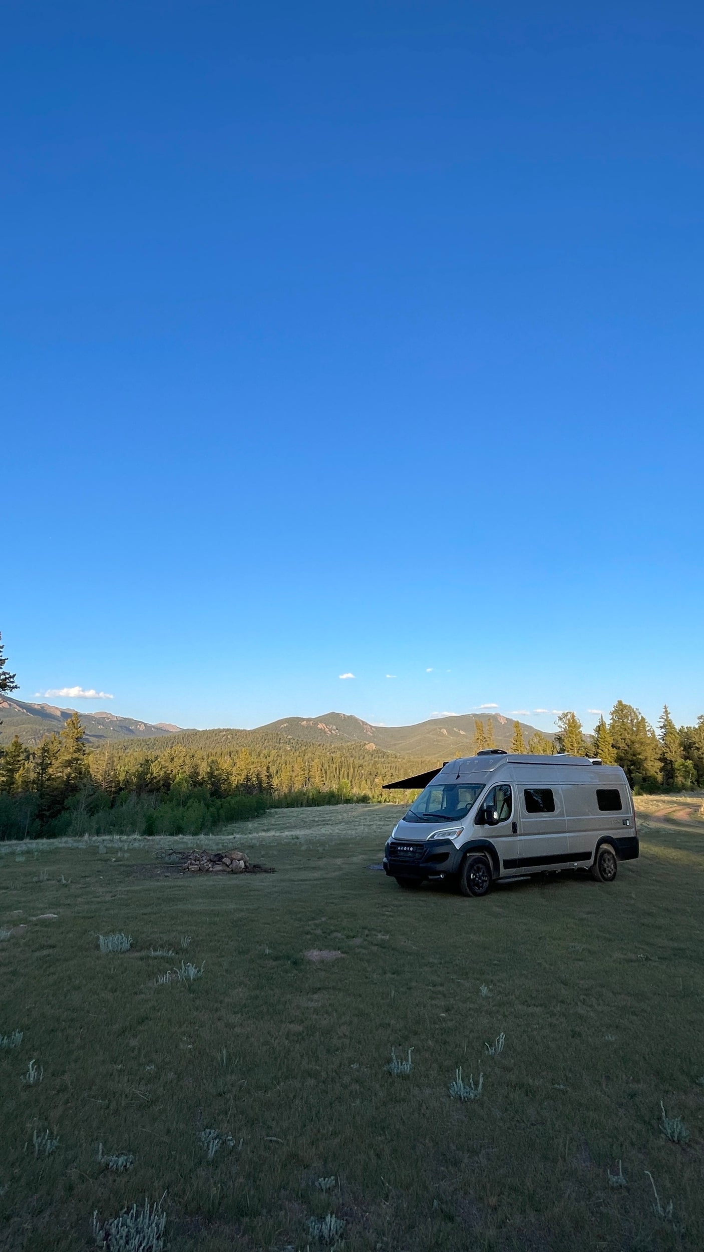 RV rental boondocking: a grey camper van with awning in a vast mountain field under a clear blue sky.